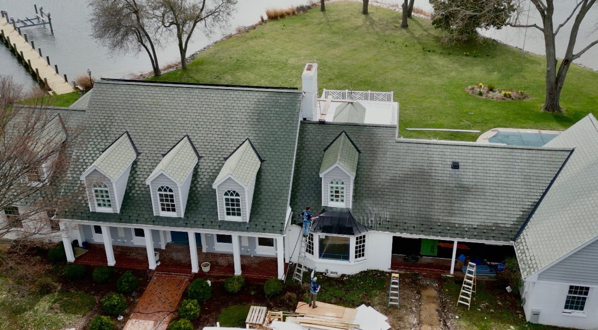 Aerial drone shot of crew soft-washing the roof of a white waterfront estate in Easton MD on Maryland's Eastern Shore by Coastal Shine