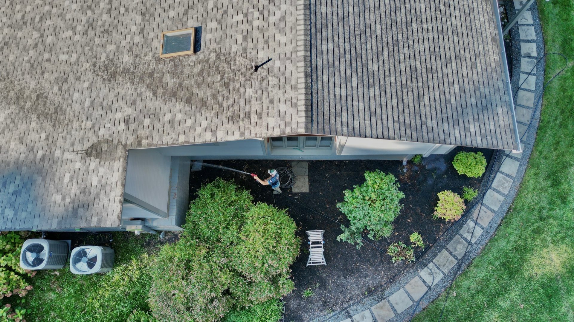 Aerial drone view of a Coastal Shine technician soft-washing a residential shingle roof and patio in Easton MD on Maryland's Eastern Shore